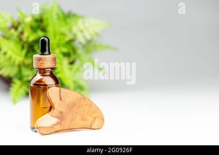 Outil de massage pour bouteille d'huile et grattoir en bois gua sha sur fond gris. Concept de soins de beauté. Copier le texte pour le texte Banque D'Images