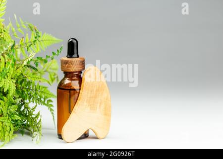 Outil de massage pour bouteille d'huile et grattoir en bois gua sha sur fond gris. Concept de soins de beauté. Copier le texte pour le texte Banque D'Images