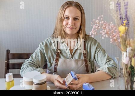 Une machine à savon pour femme prépare et emballe du savon fait main fraîchement préparé et des cosmétiques pour le soin du corps. Processus d'assemblage des commandes. Spa à la maison. Petit bus Banque D'Images