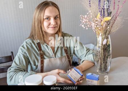 Une machine à savon pour femme prépare et emballe du savon fait main fraîchement préparé et des cosmétiques pour le soin du corps. Processus d'assemblage des commandes. Spa à la maison. Petit bus Banque D'Images