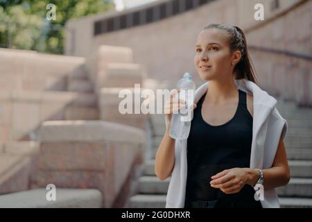 Femme avec se sent soif après l'entraînement cardio boissons eau de bouteille tient boisson rafraîchit reste hydraté poses dehors vêtu de vêtements actifs Banque D'Images