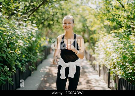 Femme a jogging entraînement courses en plein air sourires aime bonne journée vêtu de vêtements de sport écoute la musique de la liste de lecture. Commencer le jour à partir de Banque D'Images