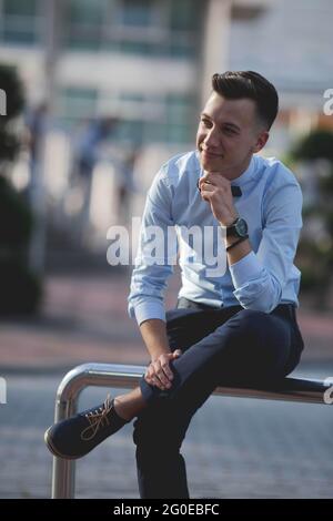 Jeune homme beau souriant et assis sur un garde-corps Banque D'Images