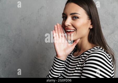Femme souriante et attirante appelant quelqu'un isolé sur fond gris Banque D'Images