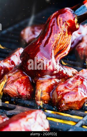 Dose verticale de côtes de bœuf désossées au gril sur les flammes avec sauce barbecue ajoutée avec une vadrouille pour barbecue. Profondeur de champ extrêmement faible avec fond flou Banque D'Images