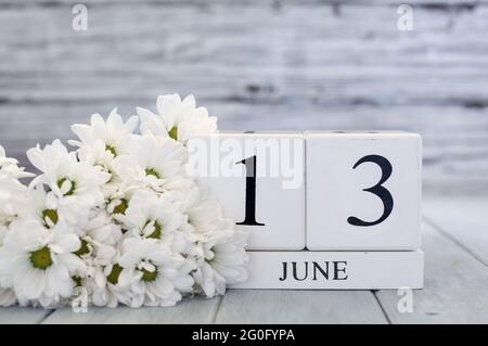 Blocs de calendrier en bois blanc avec la date du 13 juin et des pâquerettes blanches. Mise au point sélective avec arrière-plan flou. Banque D'Images