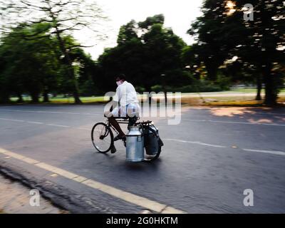 KOLKATA, INDE - 28 mai 2021 : un homme de lait transportant une très grande et petite conserve de lait sur son cycle rouillé le long d'une route urbaine Banque D'Images