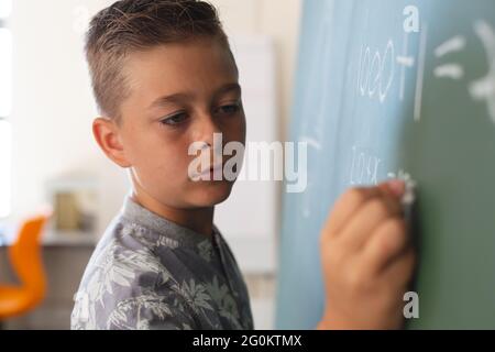 Un garçon caucasien debout au tableau de surveillance écrivant en classe pendant la leçon de mathématiques Banque D'Images