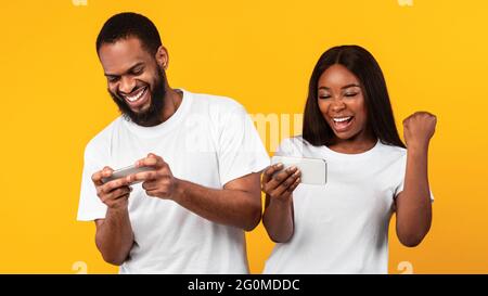 Couple afro-américain utilisant des téléphones portables, jouant au jeu Banque D'Images