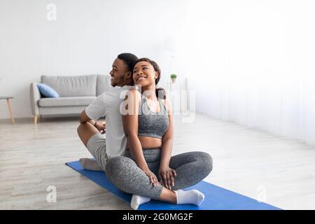 Femme noire assise dos à dos avec son petit ami sportif en position lotus, ayant la pratique de yoga de partenaire domestique Banque D'Images
