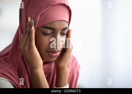 Concept de migraine. La dame noire islamique dans le hijab souffrant de maux de tête à la maison Banque D'Images