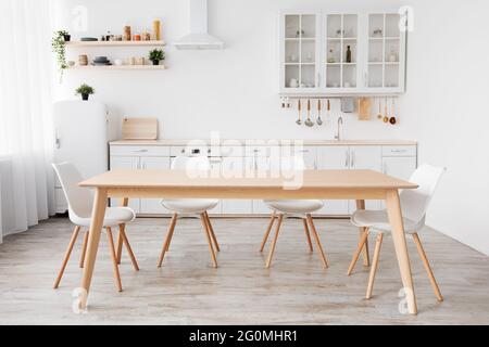 Cuisine blanche et lumineuse avec articles ménagers. Cuisine intérieure moderne, table et chaises en bois dans la salle à manger Banque D'Images