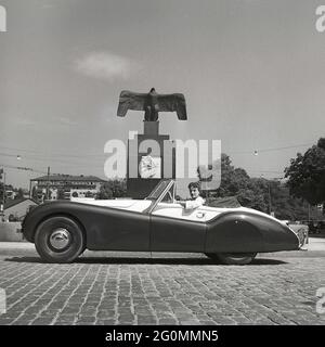 En voiture dans les années 1950. Une jeune femme dans une Jaguar XK120 décapotable ouverte. Une voiture de sport britannique qui était considérée comme ayant un design futuriste. Les chiffres 120 indiquent la vitesse de pointe de la voiture, 120 mph/193 km/h. La voiture était une deux places avec une chasse en aluminium. Il a été fabriqué en un total de 12078 voitures. Photographié dans la rue par le monument de vol de Carl Milles placé sur Karlaplan à Stockholm. Un hommage aux pilotes suédois et aux pionniers ailés. Suède 1953. Réf BL109-1 Banque D'Images