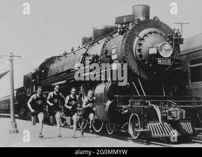 Coureurs et train dans les années 1930. Des athlètes de l'université de Californie du Sud sont en train de courir à côté d'une locomotive géante. À cette époque, cette université a remporté neuf championnats nationaux avec succès. Banque D'Images