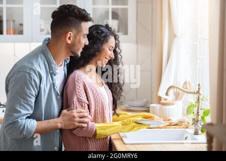 Portrait de jeunes heureux conjoints du Moyen-Orient laver la vaisselle après le déjeuner dans la cuisine Banque D'Images