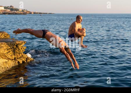 Deux gars plongée d'une falaise. Les gars musclés, le saut à la bombe et les boxers de natation Banque D'Images