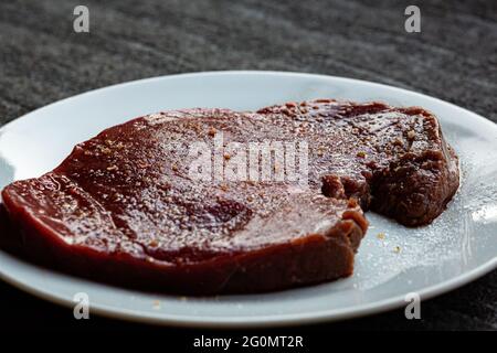 Steak cru assaisonné et salé qui se repose avant d'être cuit Banque D'Images