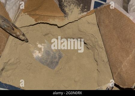 Gros plan de la truelle de plâtre dans un sac en papier entièrement ouvert de poudre de mastic pour la décoration murale, le chou-fleur ou le glaçure.concept de matériaux de construction.revêtement de finition en d Banque D'Images