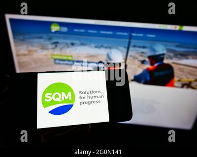 Personne tenant un téléphone portable avec le logo de la société chilienne Sociedad Quimica y Minera de Chile (SQM) à l'écran devant le site. Mise au point sur l'affichage du téléphone. Banque D'Images