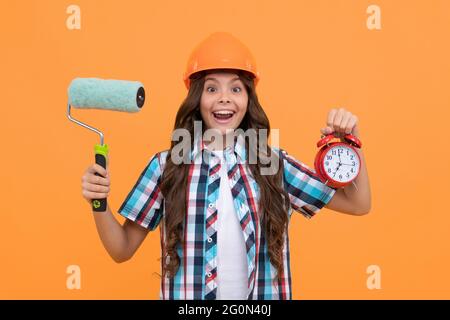 surprise adolescente tenir le rouleau de peinture et le réveil. enfant dans le casque. temps pour la décoration. Banque D'Images