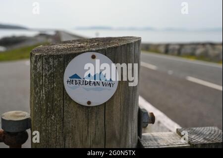 Panneau Hebridean Way sur poteau en bois. Arrière-plan fortement flou de la chaussée à Eriskay. Il s'agit d'une célèbre route à vélo et à pied. Banque D'Images