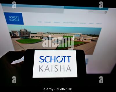 Personne tenant un téléphone portable avec le logo de la société indienne d'emballage Schott Kaisha Pvt Ltd à l'écran en face de la page web d'affaires. Mise au point sur l'affichage du téléphone. Banque D'Images