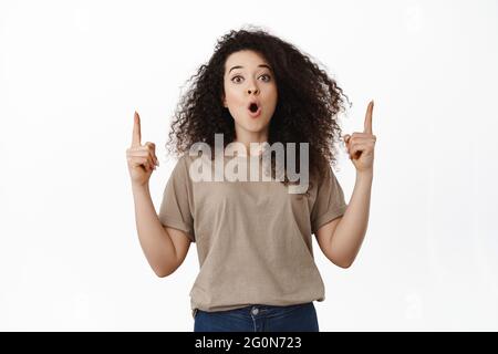 Une femme brunette impressionnée qui a fait une excellente promotion, pointant les doigts vers le haut sur la bannière de réduction et qui a l'air de dire wow surpris, recommandant le magasin Banque D'Images