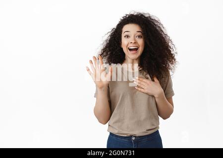 Bonjour, son moi. Bonne jeune femme qui se tient la main et s'appelle elle-même, tient la paume sur le coeur, la présente à vous, se tenant amicale et joyeuse contre le blanc Banque D'Images