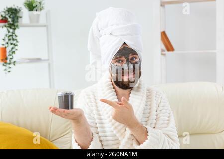 Homme barbu s'amusant avec un masque cosmétique sur son visage en argile noire. Hommes soins de la peau, humour et spa à la maison concept Banque D'Images