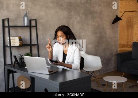 Entrepreneur féminin. Une femme d'affaires afro-américaine joyeuse travaillant sur un ordinateur portable dans un bureau moderne. Banque D'Images