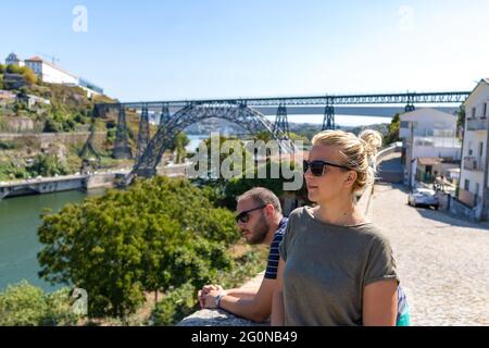 Couple touristique avec lunettes de soleil sur la pose pour une photo devant un pont d'arche Maria Pia à Porto Banque D'Images