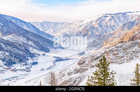 paysage enneigé d'hiver de la vallée parmi les hautes montagnes rocheuses avec une autoroute, une route et un village avec un pont au-dessus de la rivière Banque D'Images