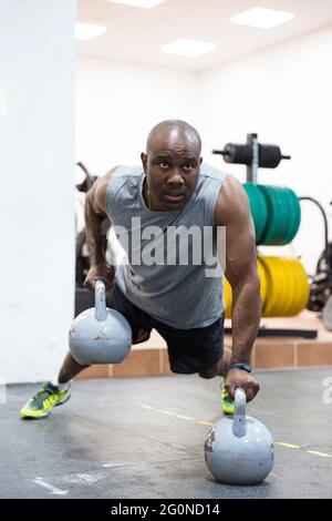 Afro-américain fort homme s'entraîner dans la salle de gym avec kettlebells. Concept de soins du corps. Banque D'Images