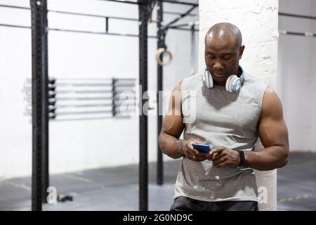 Homme noir puissant utilisant le téléphone portable dans la salle de gym. Il prend une pause. Espace pour le texte. Banque D'Images