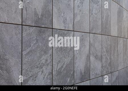 Mur incurvé situé dans un coin de rue avec carreaux gris texturés. Les joints entre les carreaux sont noirs et sont très marqués. Banque D'Images