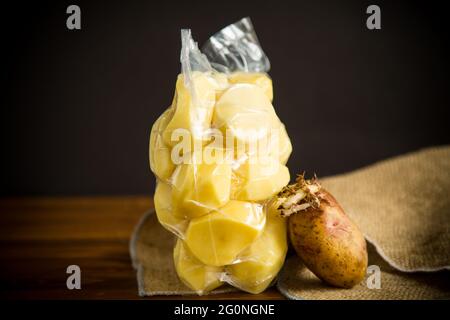 pommes de terre pelées fermées dans un sac à vide et vieilles pommes de terre germées sur une table en bois Banque D'Images