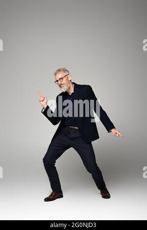 homme d'âge moyen en lunettes et costume dansant sur le gris Banque D'Images