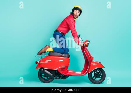 Pleine taille profil photo de côté de jeune funky drôle choqué homme équitation moto isolé sur fond turquoise couleur Banque D'Images