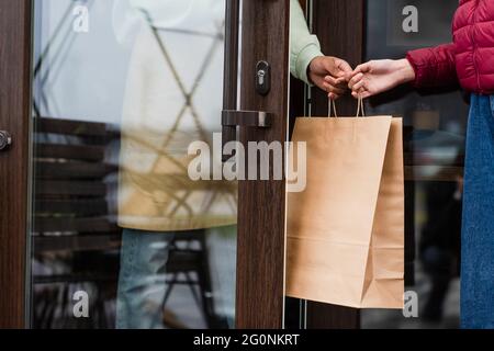 Vue rognée du barista afro-américain qui donne un sac en papier au client près de la porte du café Banque D'Images