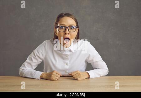 Bonne surprise femme d'affaires dans des verres assis au bureau et regardant l'appareil photo Banque D'Images