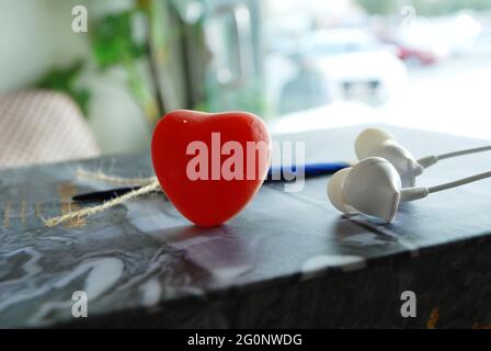 coeur en gelée rouge avec plumes bleues et écouteurs isolés papier ondulé marbré, arrière-plan flou de jour, papier peint romantique, espace pour qoutes et texte Banque D'Images