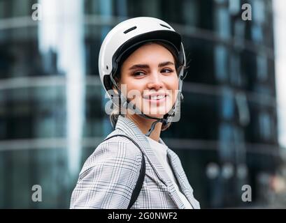 Portrait d'une femme souriante portant un casque de cyclisme debout devant un immeuble de bureaux Banque D'Images
