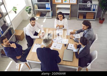 Une équipe de jeunes travailleurs à l'écoute du cadre supérieur assis autour de la table du bureau lors d'une réunion d'entreprise Banque D'Images