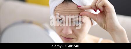 La femme examine ses rides du front dans le miroir Banque D'Images