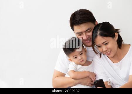 Joyeux jeune famille asiatique avec son fils riant en regardant des vidéos amusantes sur smartphone, les parents avec des enfants aiment jouer à des jeux ou de divertissement en utilisant mobi Banque D'Images