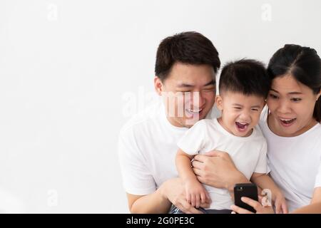 Joyeux jeune famille asiatique avec son fils riant en regardant des vidéos amusantes sur smartphone, les parents avec des enfants aiment jouer à des jeux ou de divertissement en utilisant mobi Banque D'Images