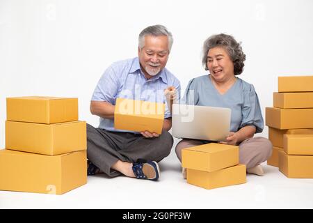 Asiatique senior couple démarrage petite entreprise freelance avec boîte à colis et ordinateur portable et assis sur le sol isolé sur fond blanc, Online mar Banque D'Images