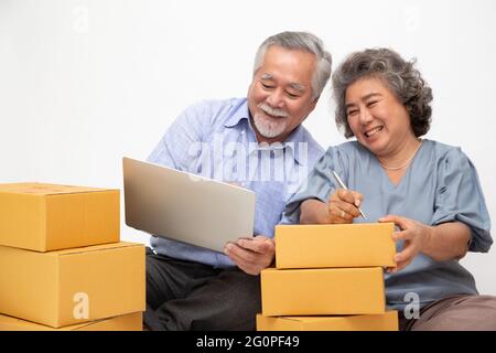 Asiatique senior couple démarrage petite entreprise freelance avec boîte à colis et ordinateur portable et assis sur le sol isolé sur fond blanc, Online mar Banque D'Images