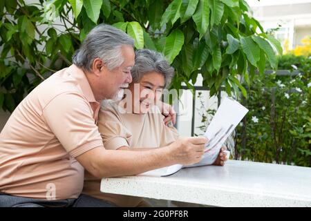 Un couple asiatique âgé riait en lisant le journal sur la table à l'extérieur, à la maison du jardin devant Banque D'Images