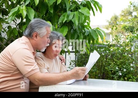 Un couple asiatique expérimenté et enthousiaste se sentant stupéfié par de bonnes nouvelles surprises lors de la lecture de journaux ou de magazines dans la maison du jardin devant Banque D'Images